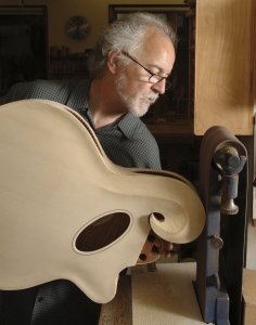 Luthier John Monteleone holds an unfinished body of a guitar to a sanding belt